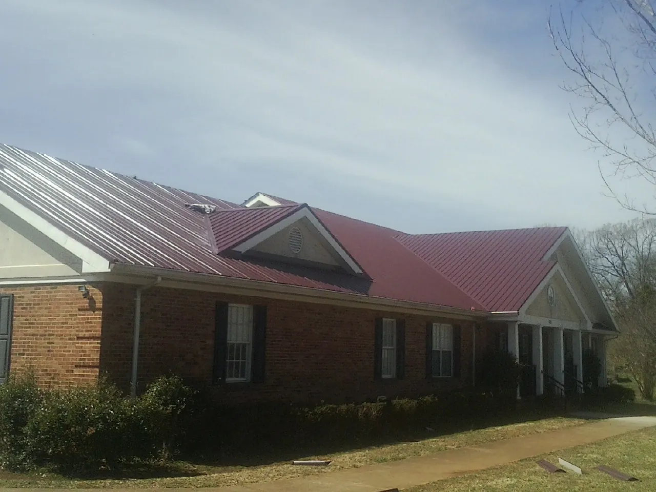 Red metal roof with gabled entries on a long brick building, from a Hail Damage Roof Repair job in Alviso