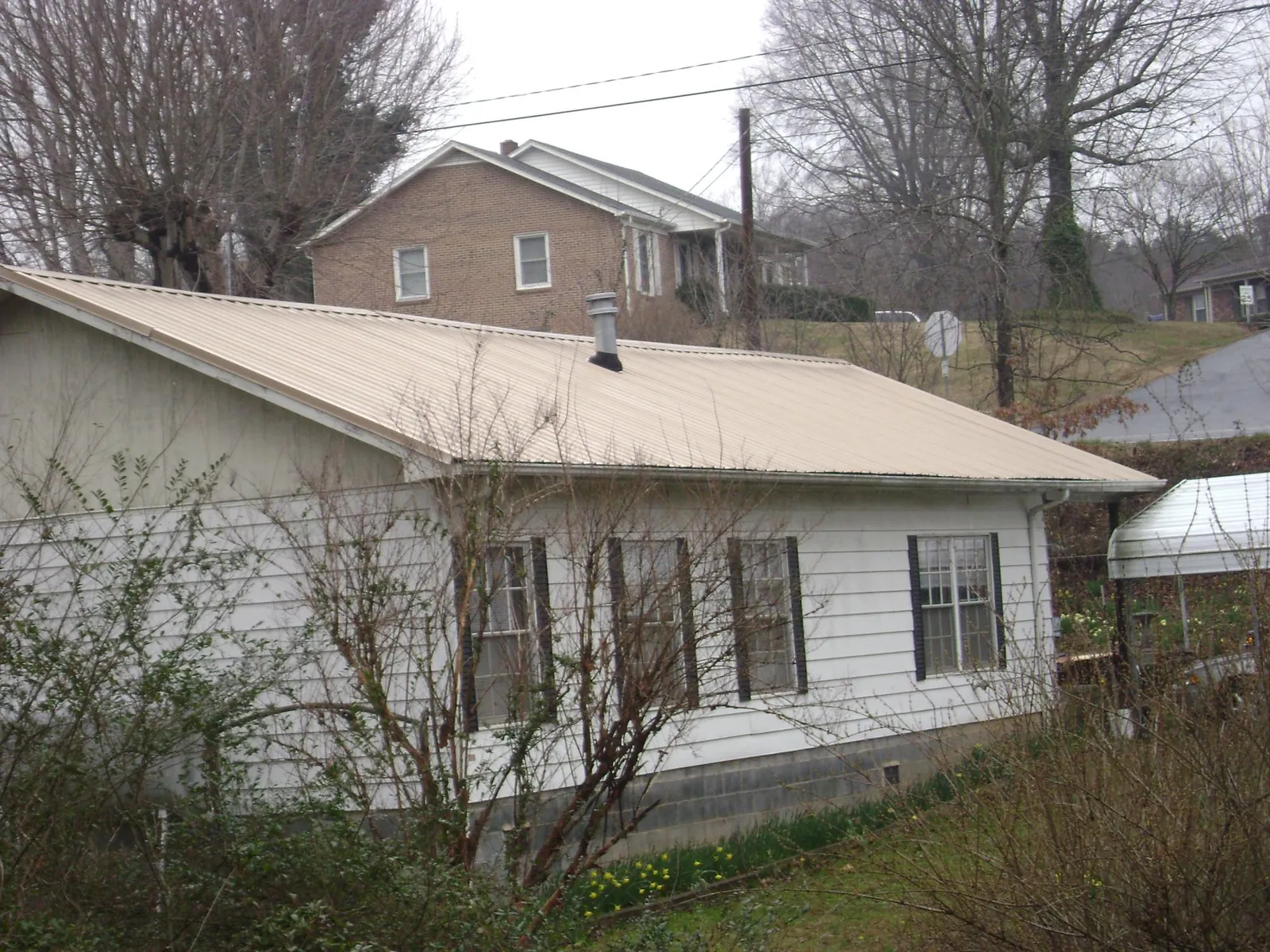 Tan metal roof on a white sided house set into a hillside — Commercial Roofing by Roofing Brothers in Alviso